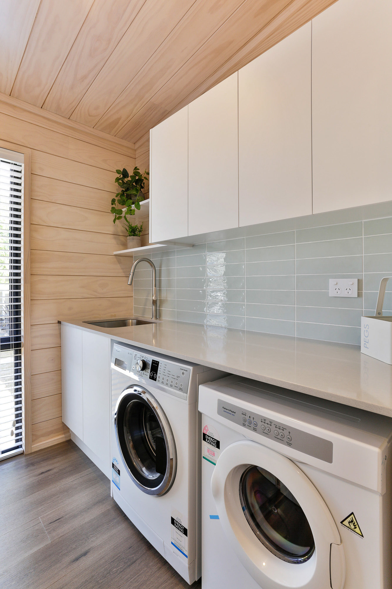 Lockwood laundry with soft blue tiles and white overhead cupboards in Wellington